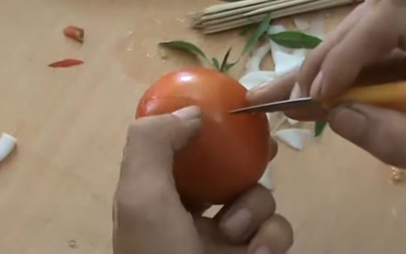 Using a knife to make a light cut to split the tomato in half